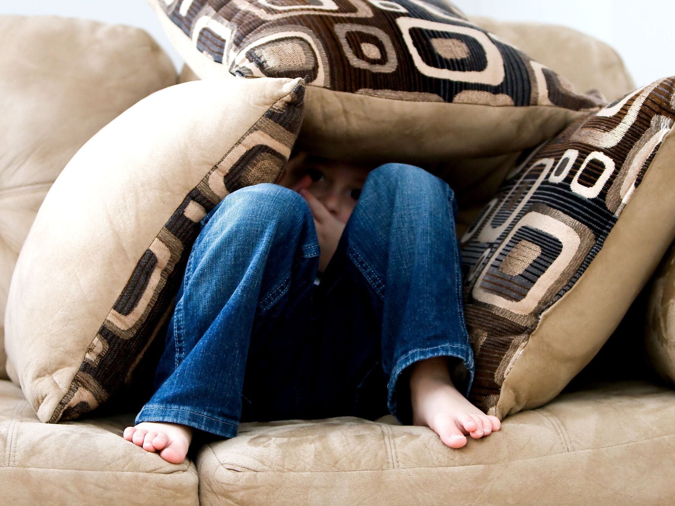 A child crouched under cushions on a couch, conveying a sense of playfulness or fear.