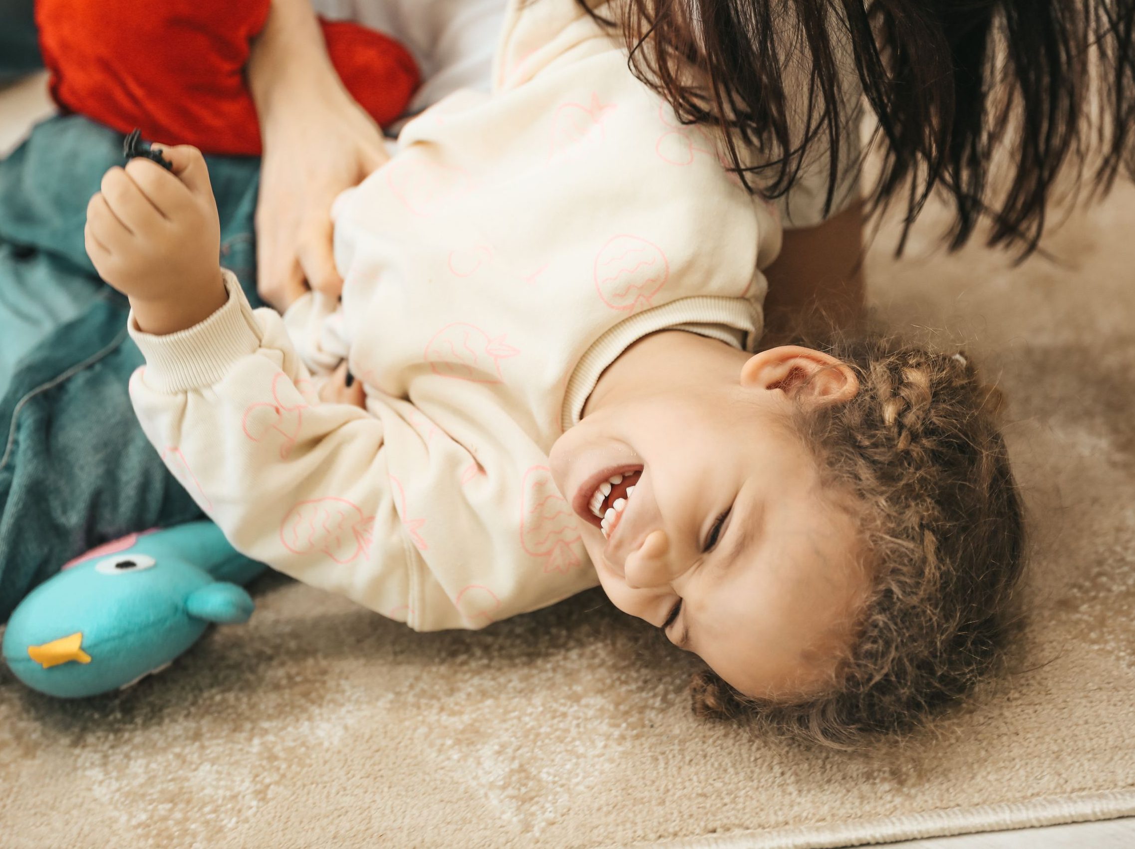 A happy child laughs while playing with a parent indoors, capturing pure joy and innocence.