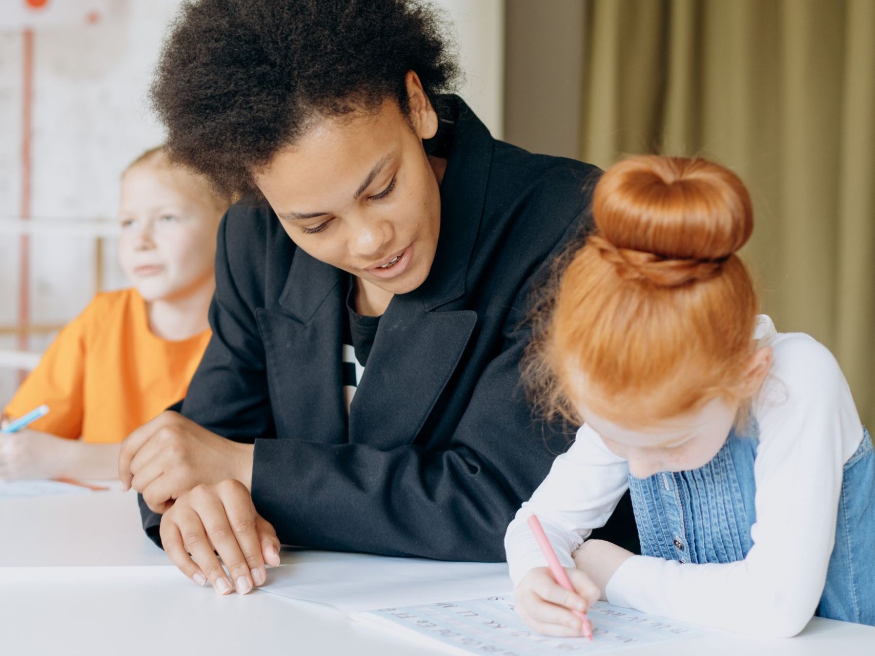 A teacher helps her young students with assignments in a bright classroom.