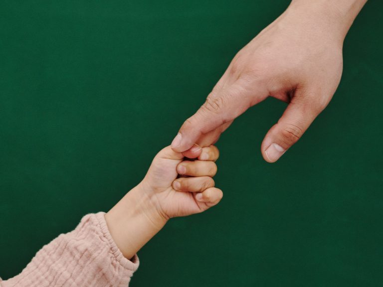 A touching moment of adult and child holding hands with green backdrop.