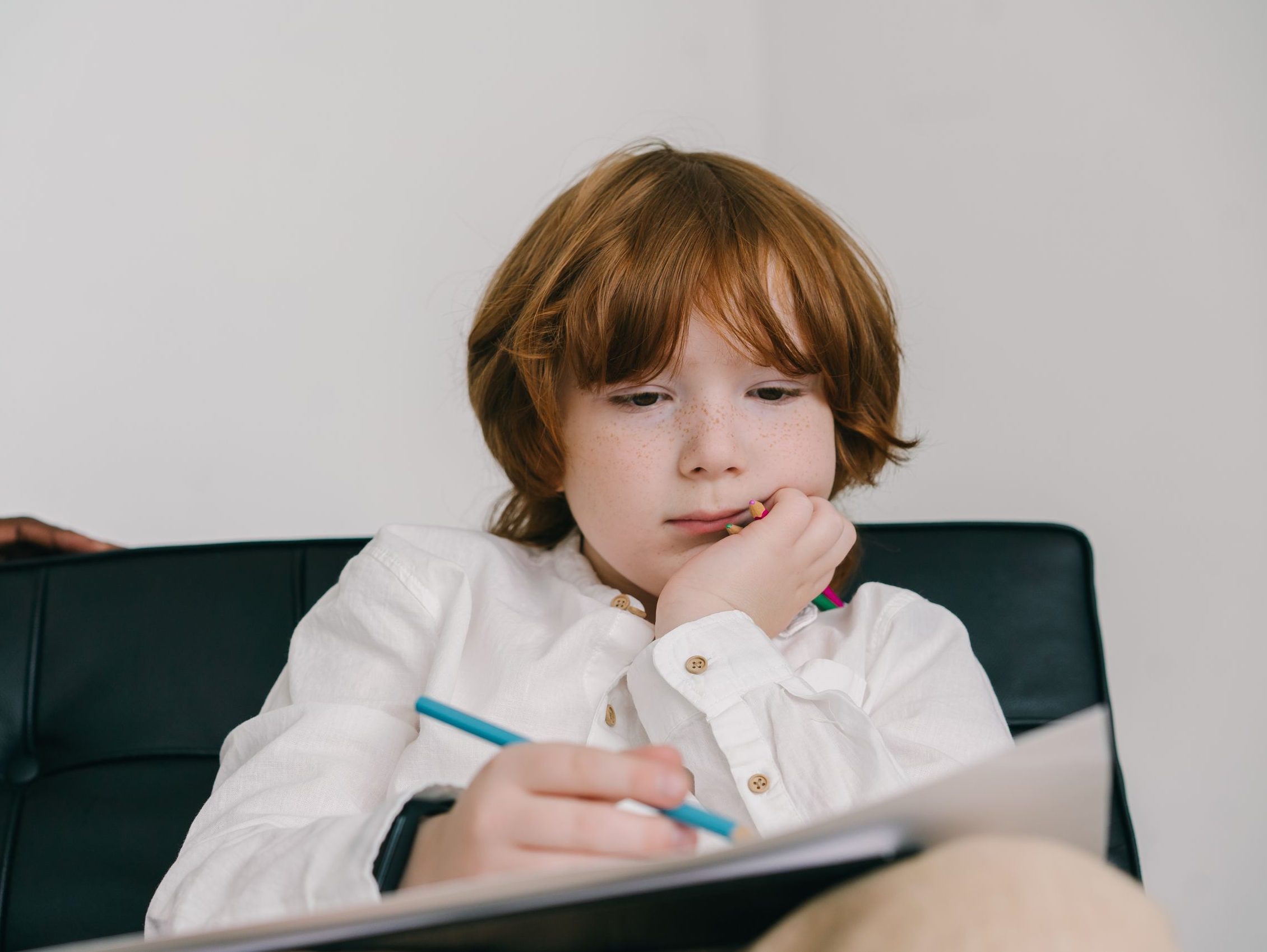 A young boy with red hair concentrating on drawing, displaying focus and creativity.