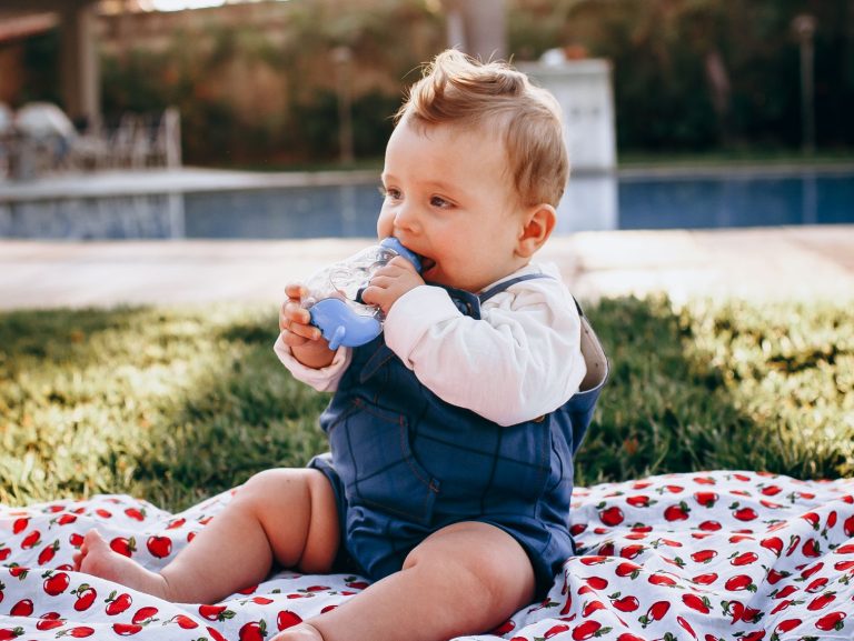 Adorable baby sitting on a blanket outdoors, playing happily in the sunlight.
