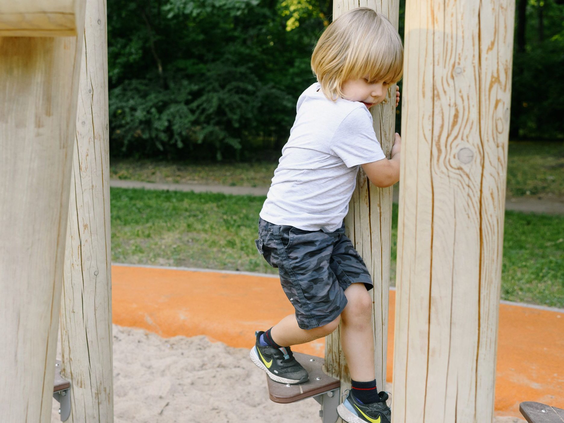 Young boy climbing a wooden playground structure in a park on a sunny day, having fun and enjoying outdoor play.