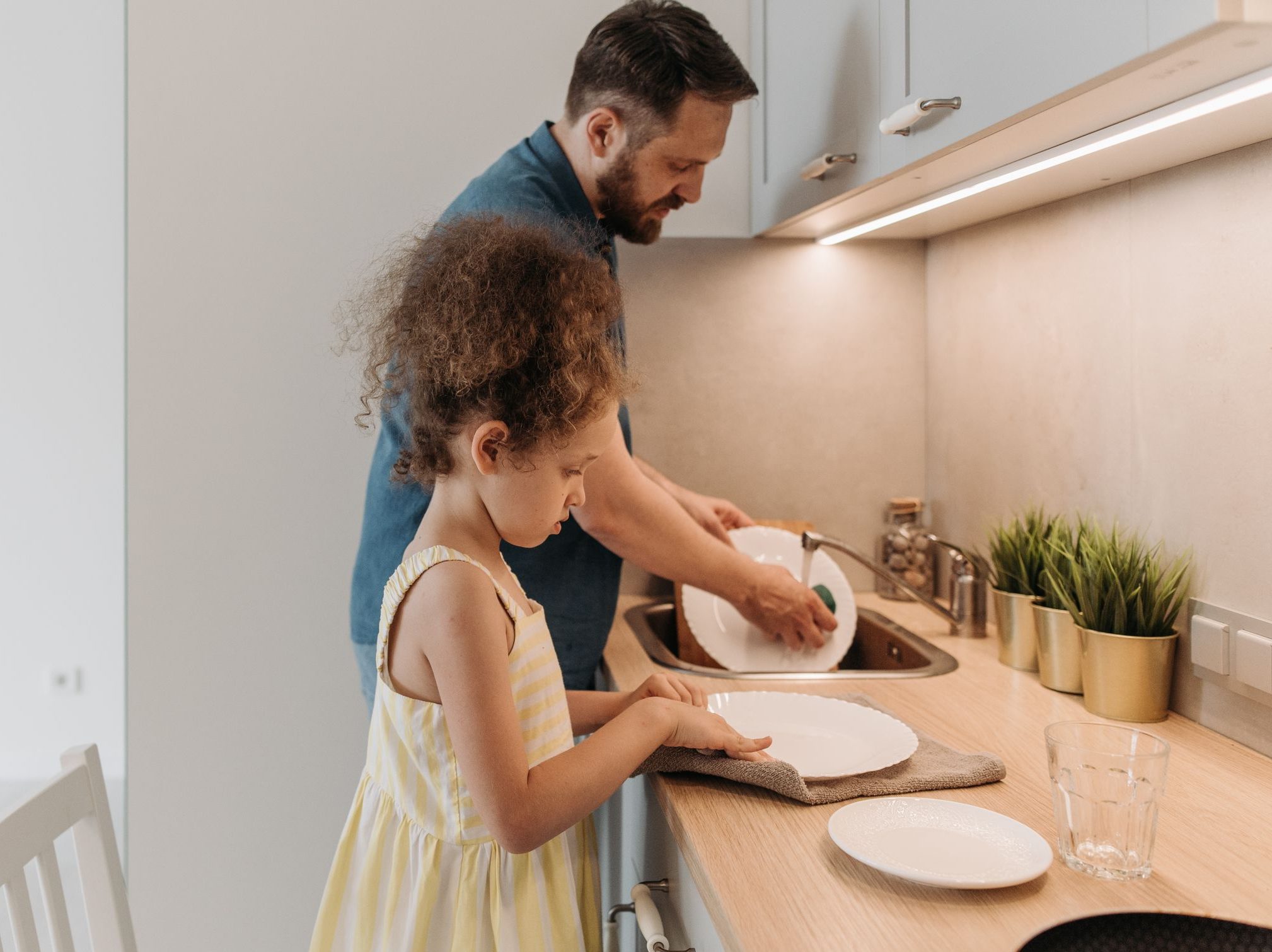 Father and daughter bonding while washing dishes together in a modern kitchen.