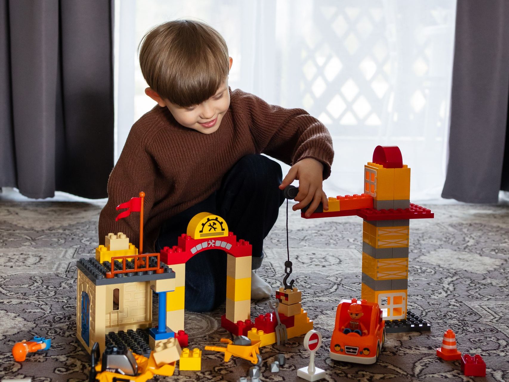 Young boy enjoying building with colorful toy blocks on the floor inside.