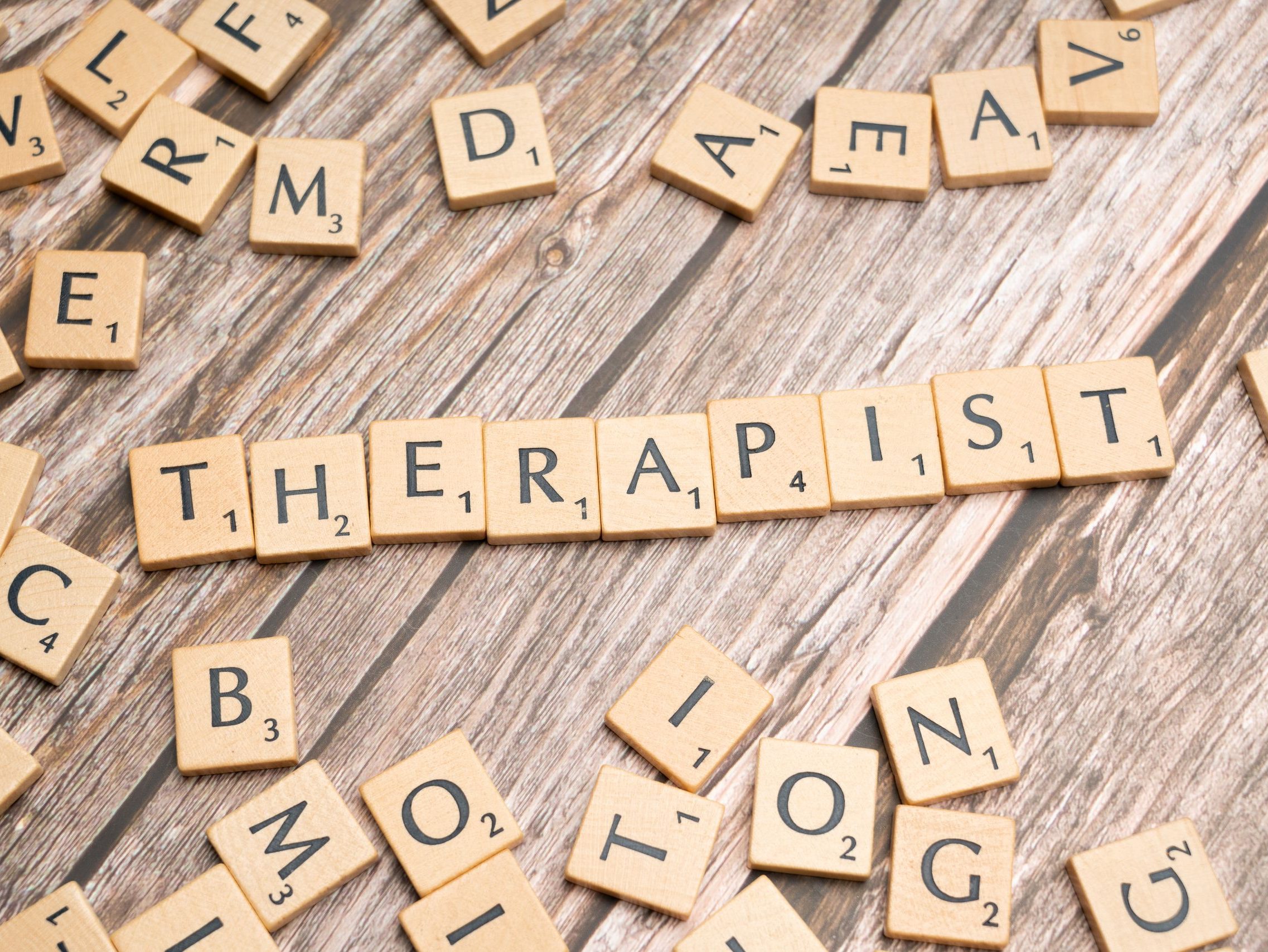 Wooden letter tiles on a rustic surface spell the word 'Therapist'.